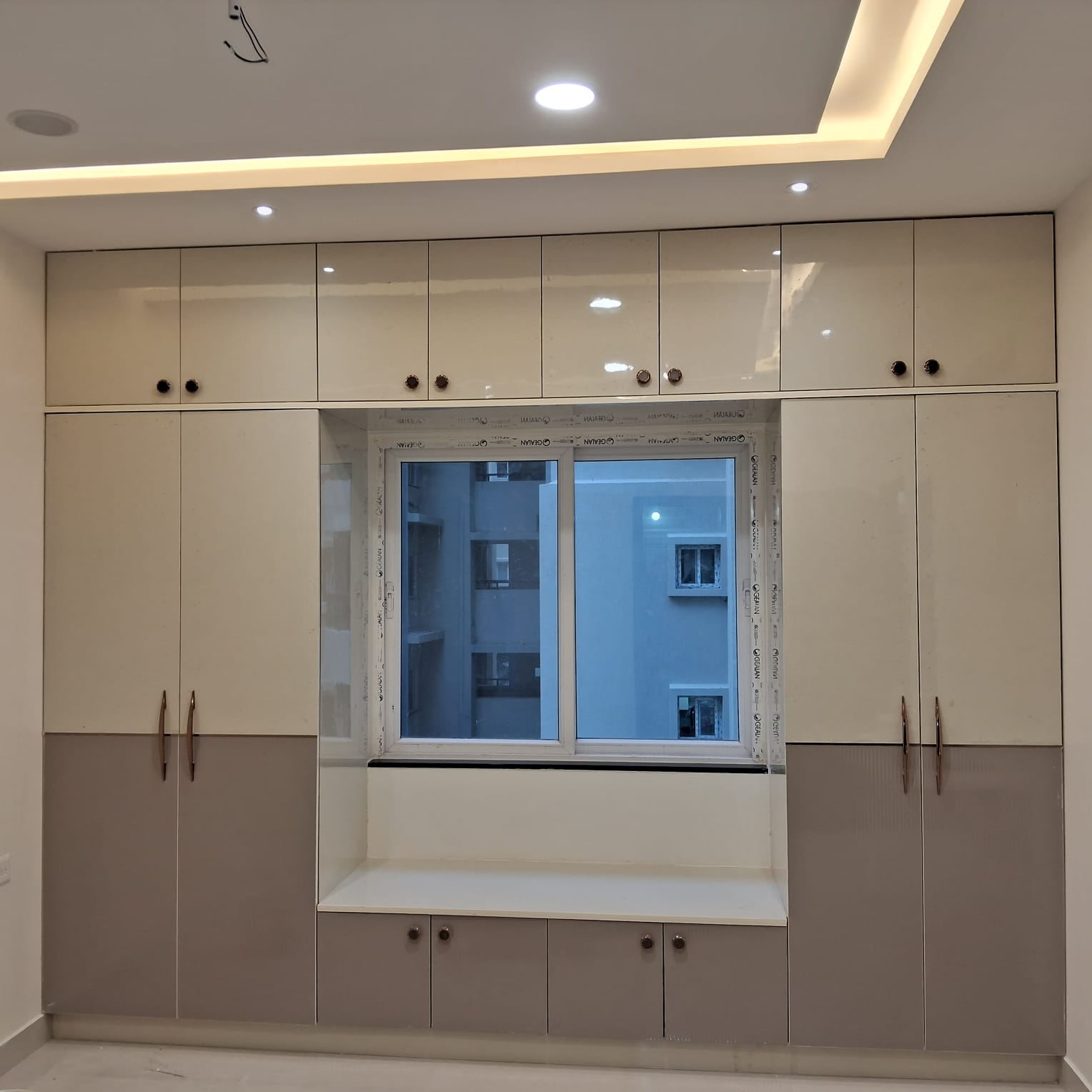 Fitted wardrobe wrapping a window seat in cream and grey
