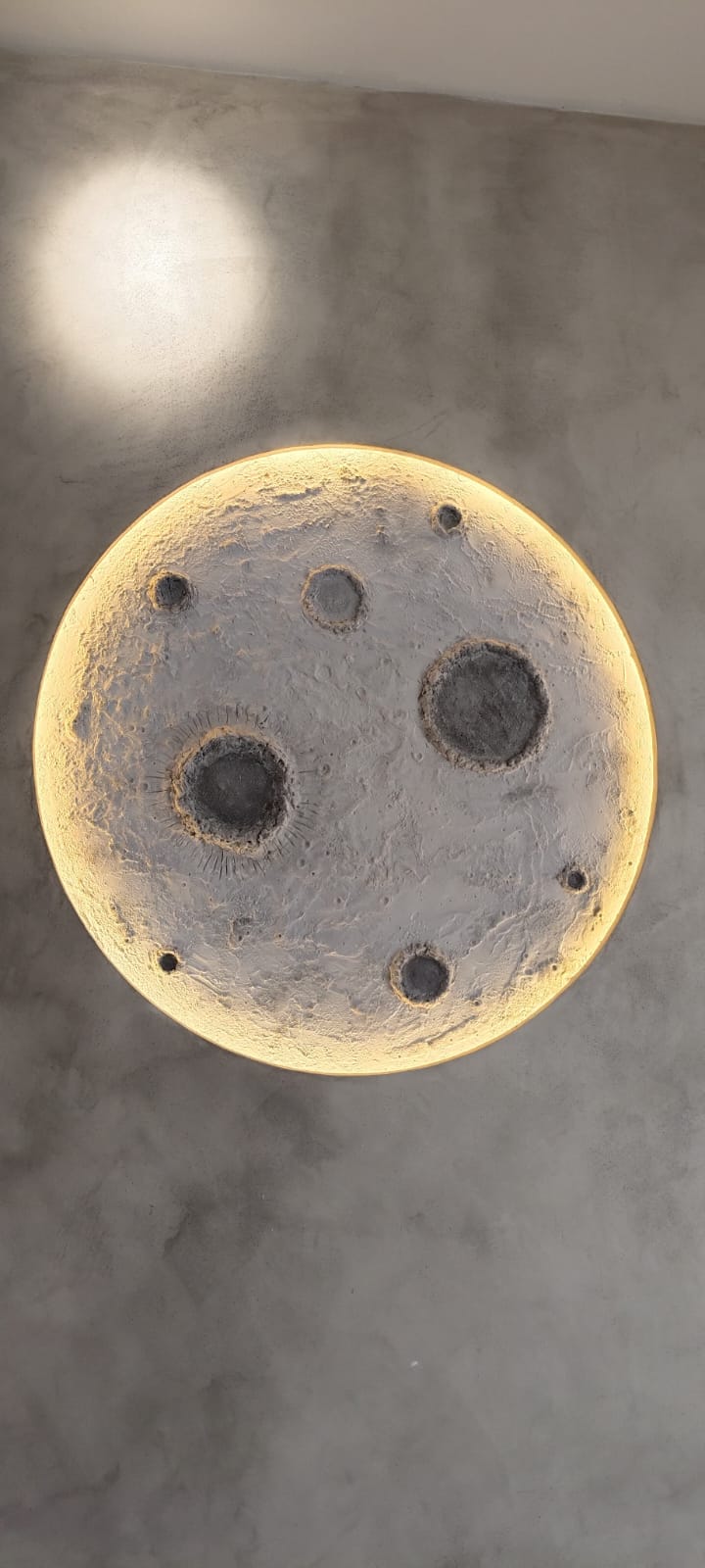 Backlit sculptural moon-crater wall light on raw concrete wall